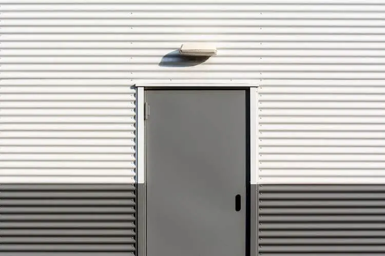 Drzwi aluminiowe w elewacji przemysłowej z blachy falistej – minimalistyczny, nowoczesny design.